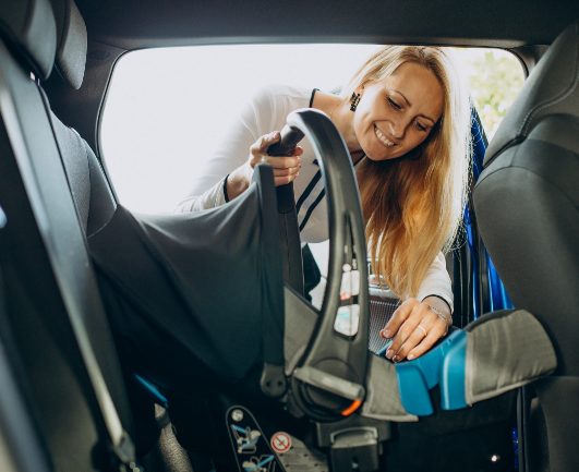 A woman placing her babyseat in the back of a car that's rented by 123 Car Rental Bonaire