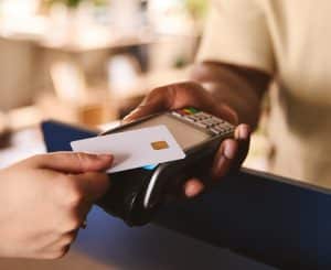 Close In Of Sales Assistant In Retail Shop With Customer Paying Using Contactless Payment Credit Card NFC